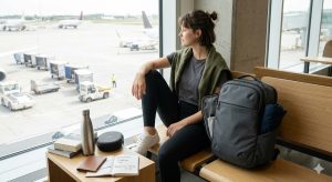 Jeune femme en tenue de voyage confortable assise à côté de son sac à dos cabine minimaliste dans un terminal d'aéroport lumineux.