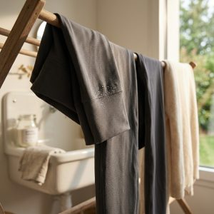 Legging technique premium de couleur anthracite séchant à l'air libre sur un étendoir en bois, mettant en valeur des gouttelettes d'eau sur la fibre thermorégulatrice